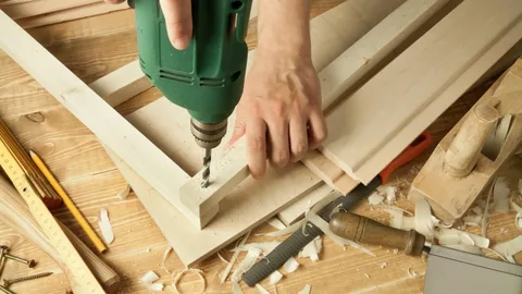 Expert carpenter drilling a wooden frame on a workbench to build a bespoke custom bathroom vanity unit.